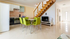 A modern kitchen with a dining area, a wooden staircase, and a flat-screen TV.