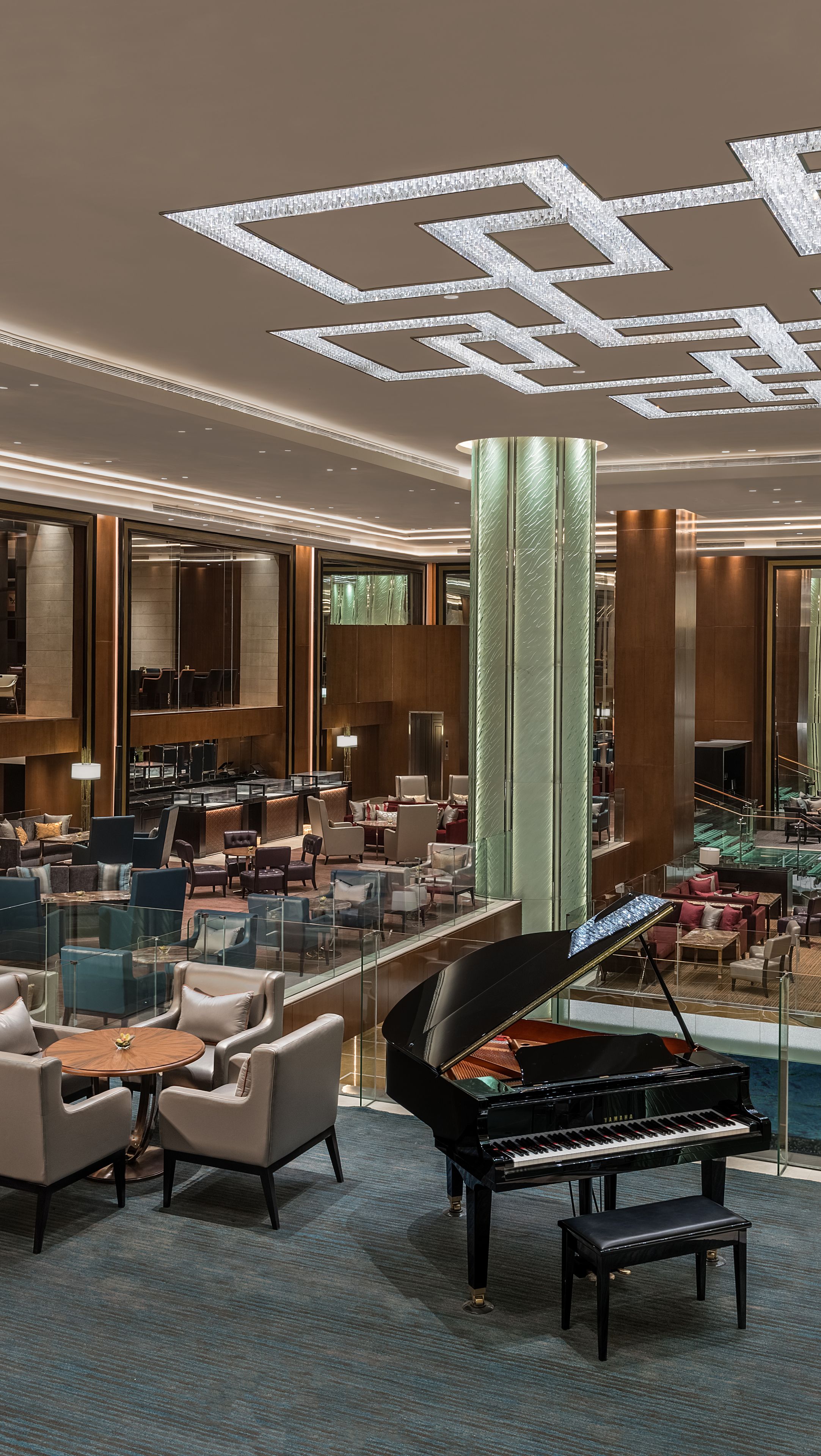 A spacious lobby with a grand piano, comfortable seating, and a modern chandelier.