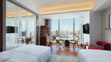 A modern hotel room with two beds, a dining area, a TV, and a city view.