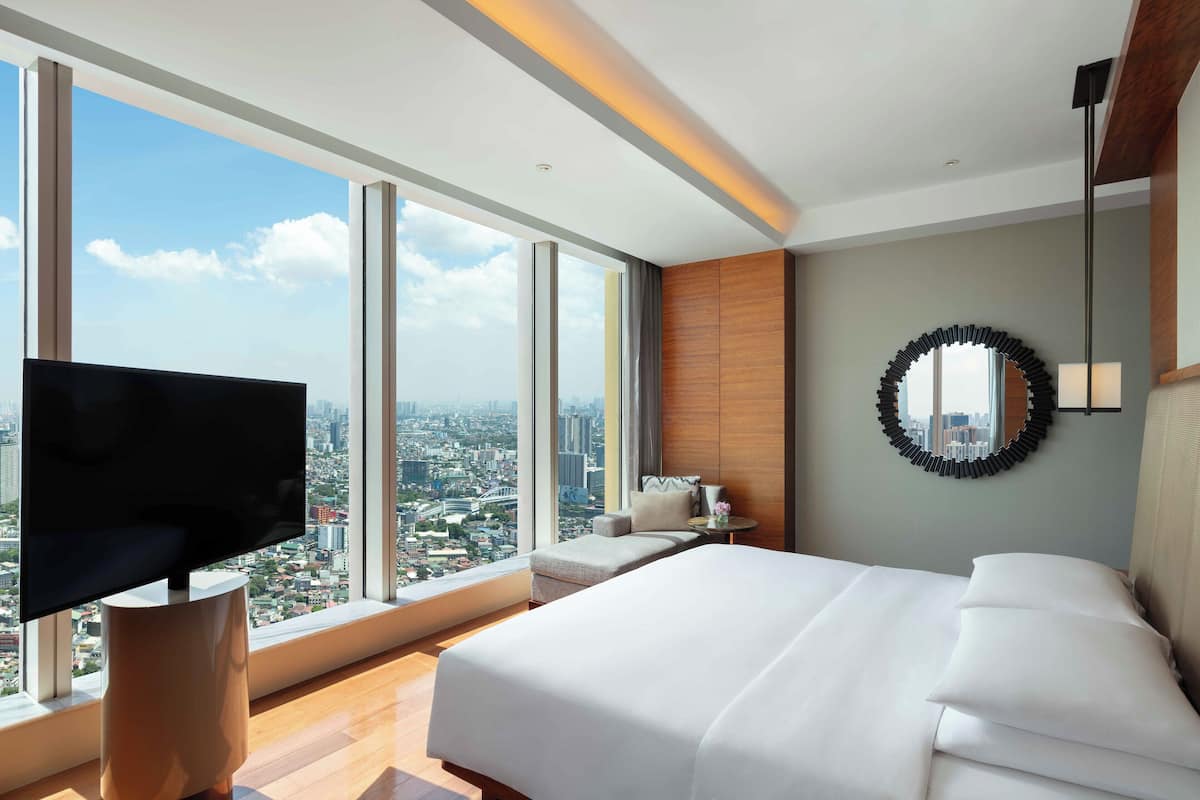 A modern hotel room with a large bed, a TV, and a city view.