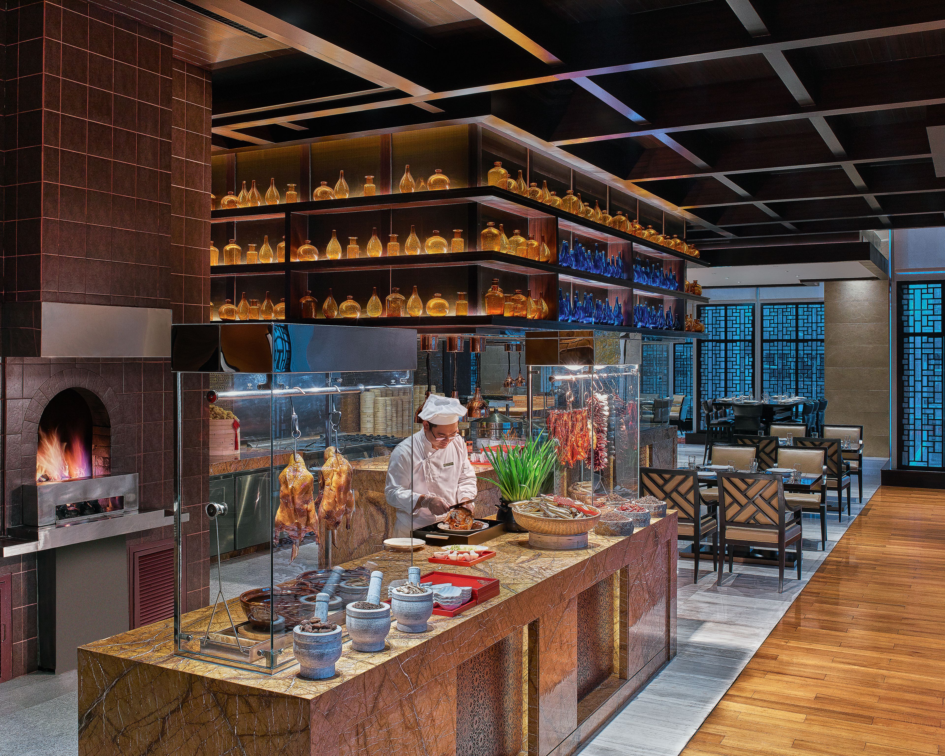 A restaurant with a chef preparing food, a display of bottles, and a traditional stove.