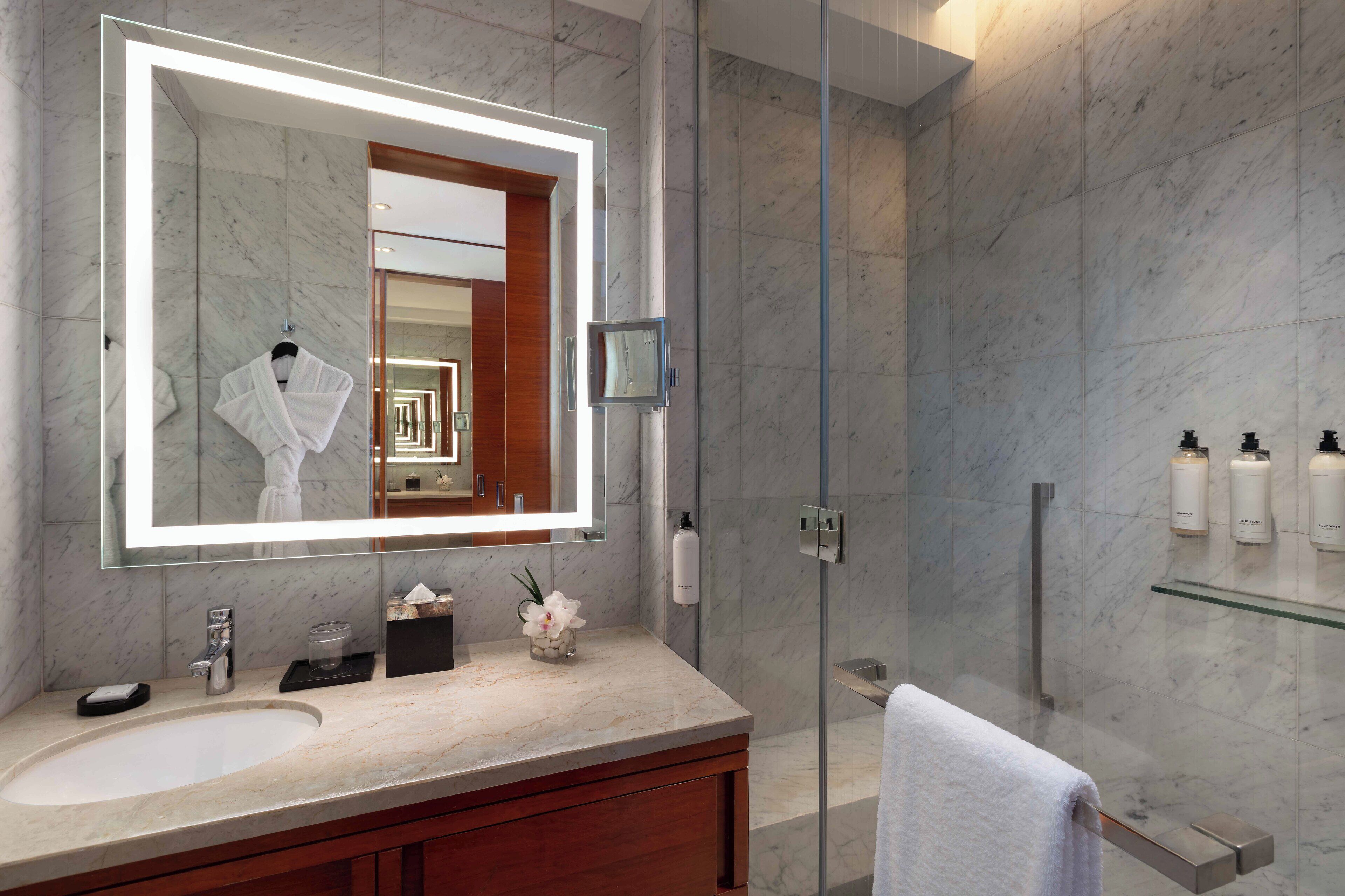 A modern bathroom with a large mirror, a glass shower enclosure, and marble countertops.