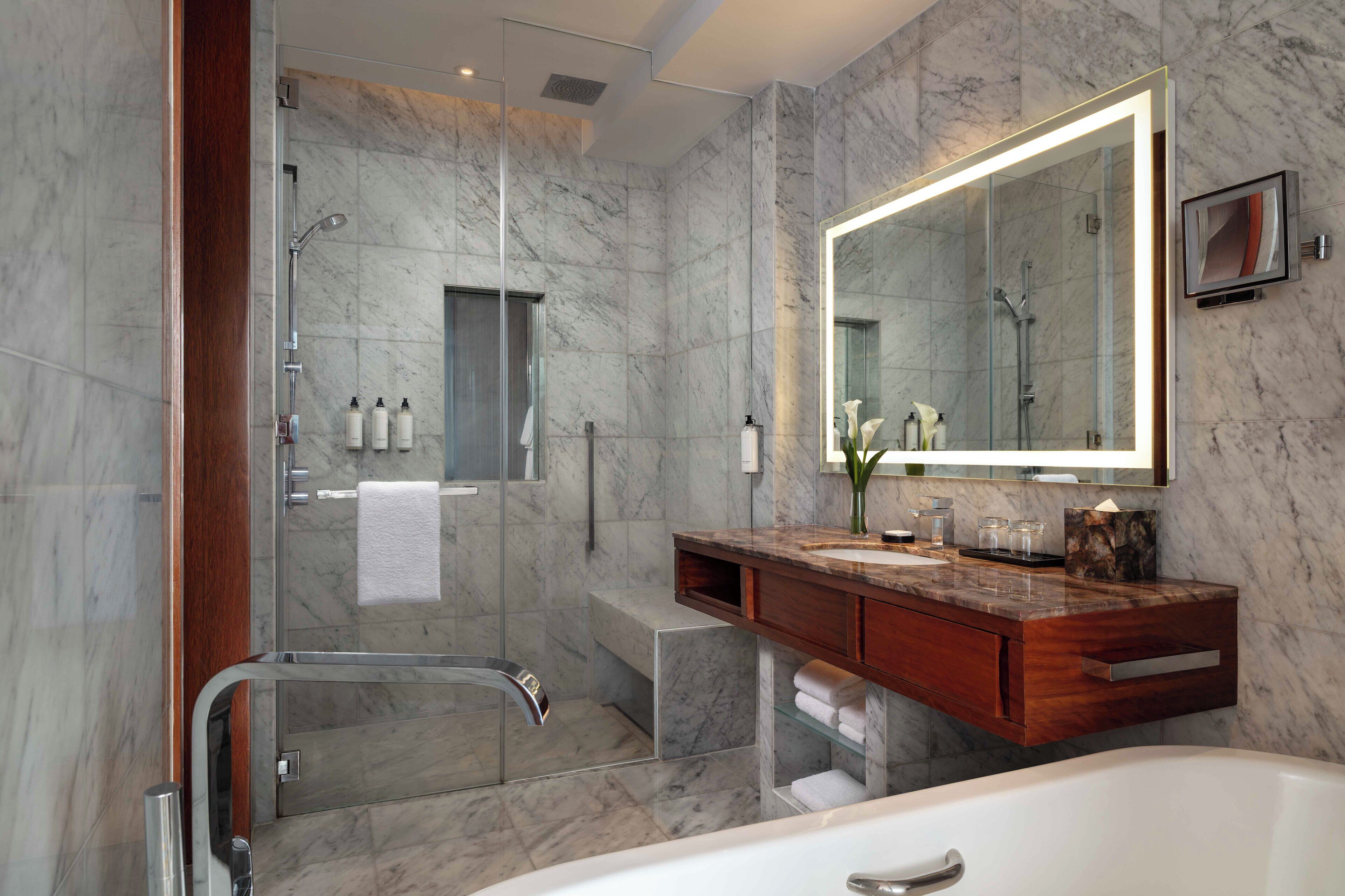 Un baño moderno con cabina de ducha acristalada, pared con azulejos de mármol, tocador de madera y un espejo grande.