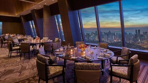 Habitación de hotel en un rascacielos con una vista panorámica de la ciudad, una mesa redonda dispuesta para una comida, y un gran ventanal con vistas al paisaje urbano.