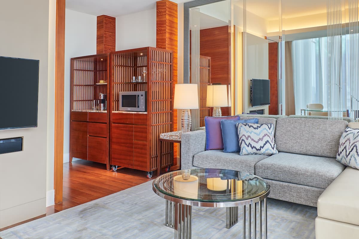A modern living room with a grey sofa, a glass coffee table, a wooden cabinet, and a flat-screen TV.