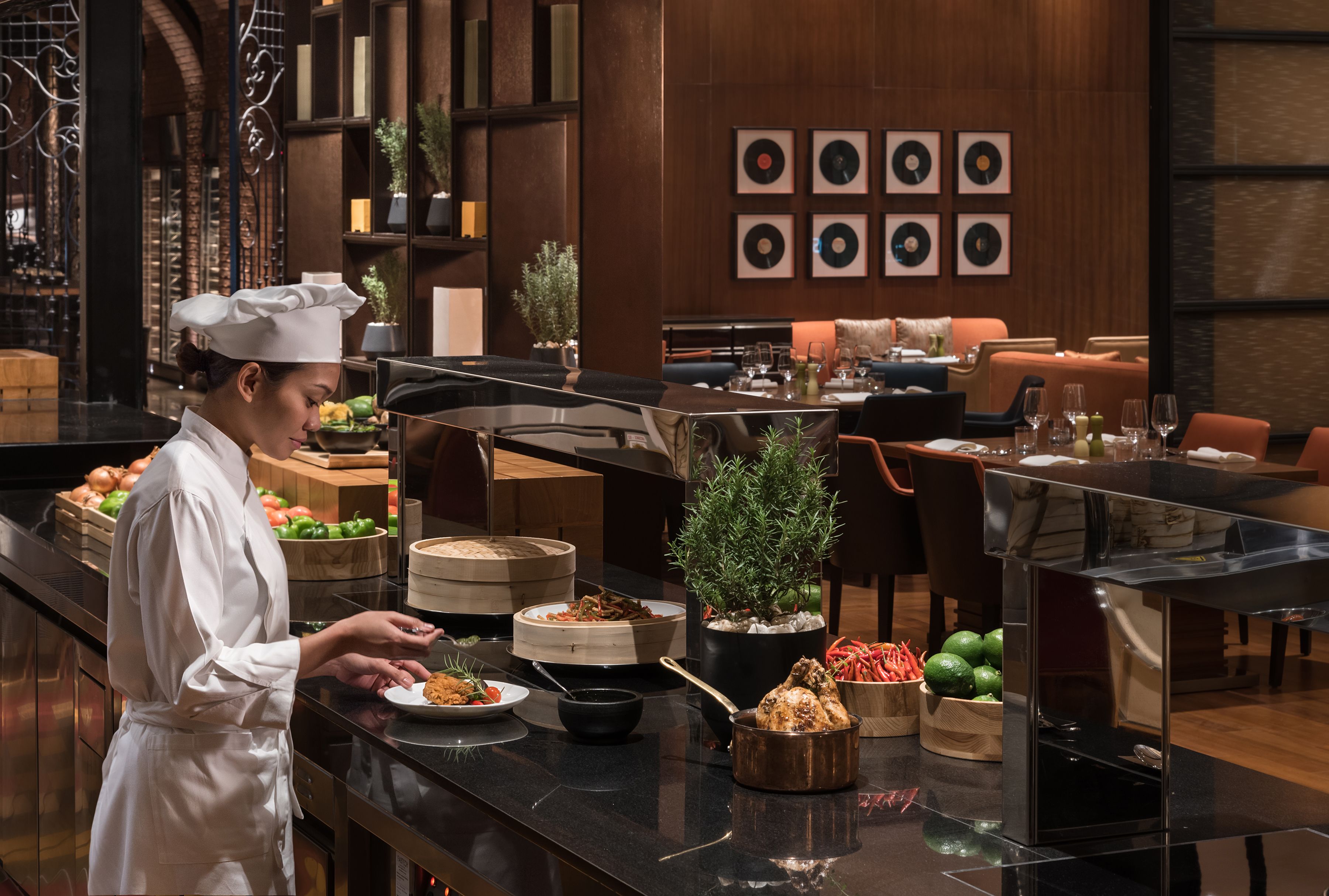 A chef preparing food in a modern restaurant with a counter, various dishes, and a dining area with tables and chairs.