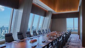Uma sala de conferências com uma mesa comprida, várias cadeiras e vista para a cidade através de grandes janelas.