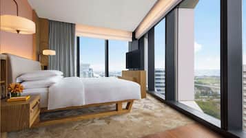 A modern hotel room with a large bed, a TV, and a city view.