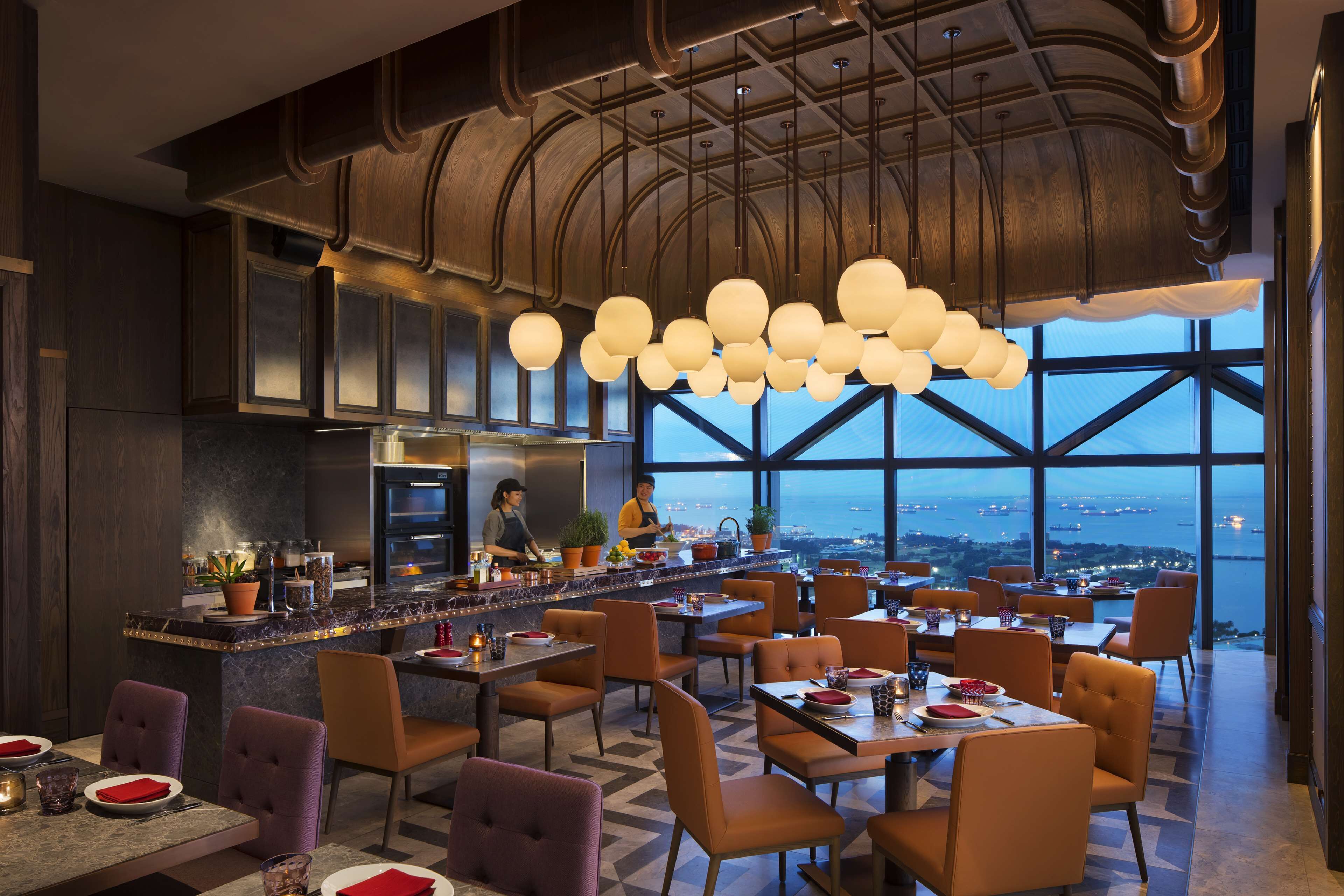 Ein modernes Restaurant mit hoher Decke, großen Fenstern und einer zentralen Bar.