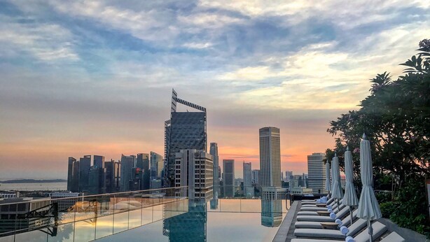 A rooftop infinity pool with lounge chairs and umbrellas, overlooking a city skyline at sunset. - ANDAZ SINGAPORE, BY HYATT (Singapore)