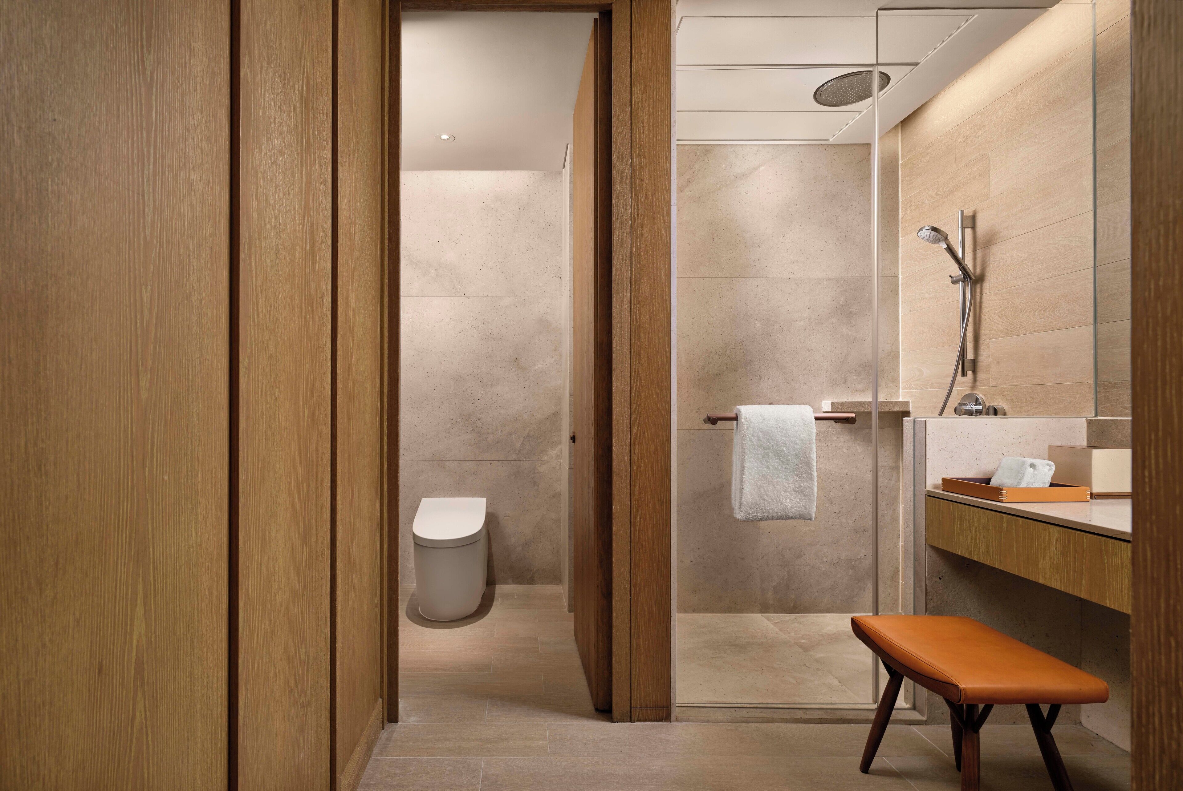 A modern bathroom with a wooden vanity, a glass shower enclosure, and a bench.
