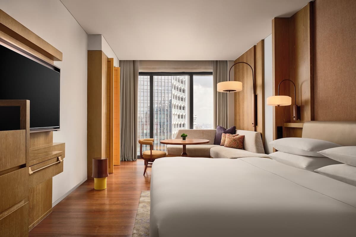 A modern hotel room with a large bed, a sofa, a small round table, and a TV.