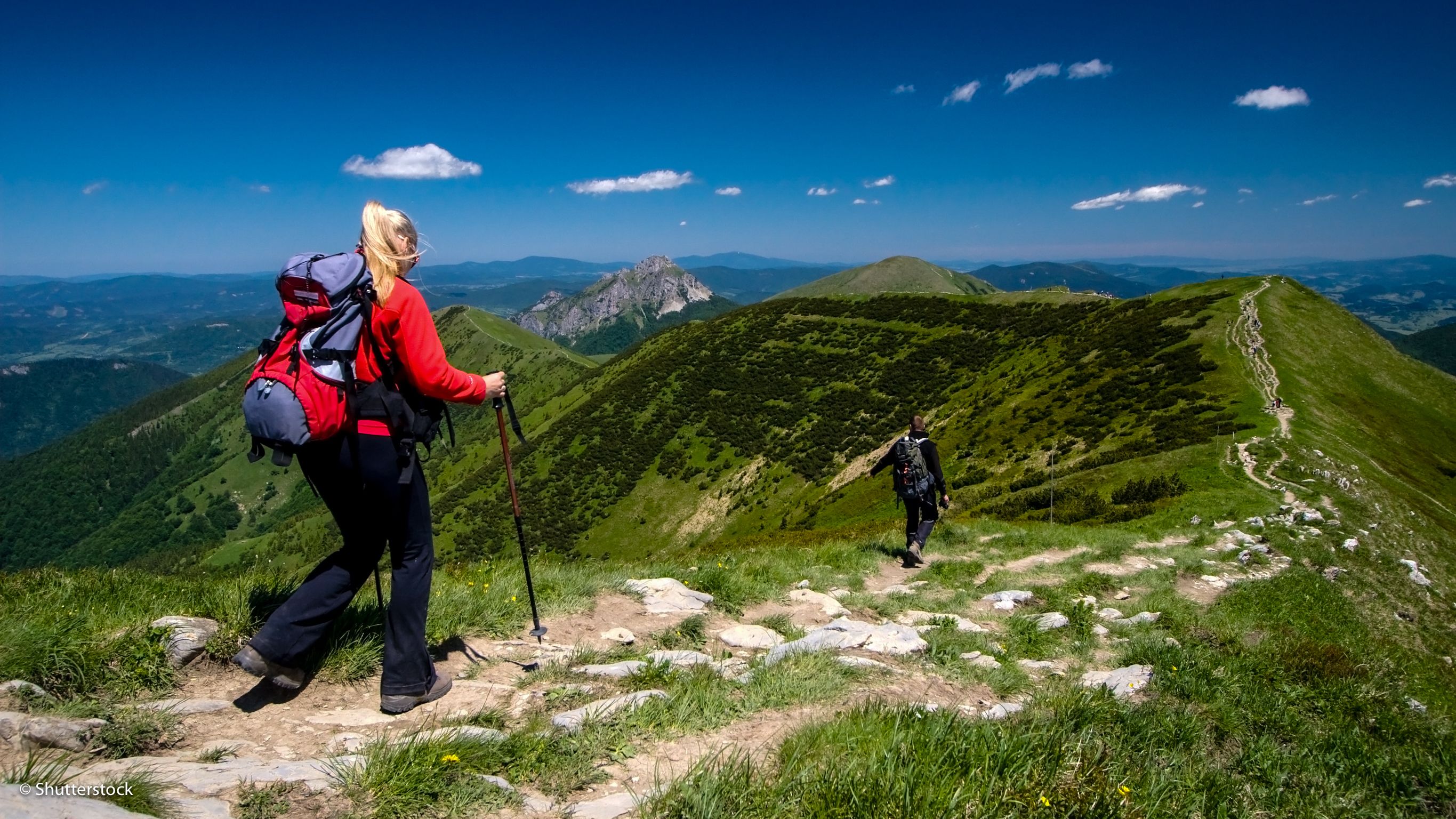 A hiker on a mountain trail with a clear view of the surrounding landscape.