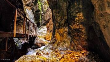 A rustic wooden bridge over a flowing stream in a rocky gorge.
