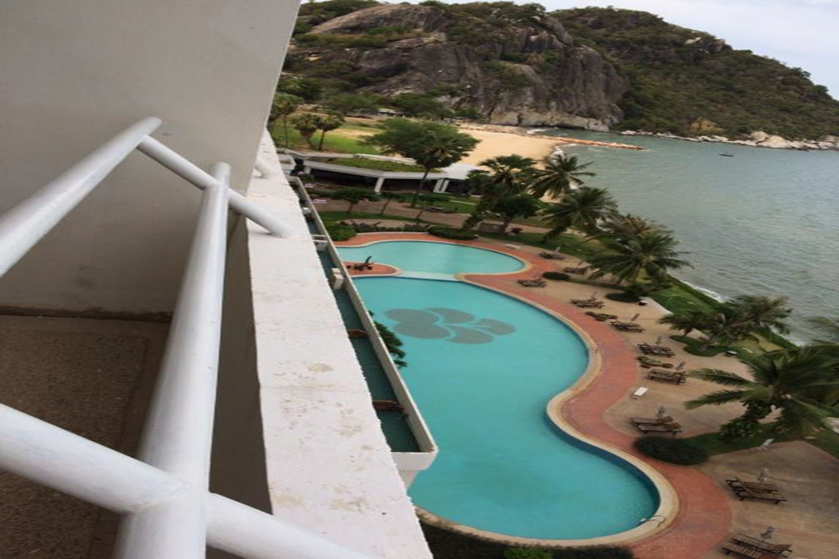 Piscina com design floral, rodeada por palmeiras e vista para a praia.