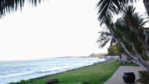 A coastal walkway with a view of the ocean, a concrete path, and a large black planter.