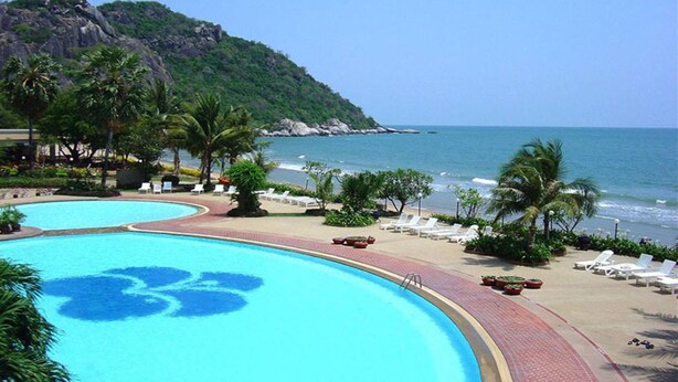 A resort pool with a tropical setting, surrounded by palm trees and a beach view.