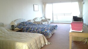 A hotel room with two beds, a desk, a chair, a laptop, and a balcony with a railing.