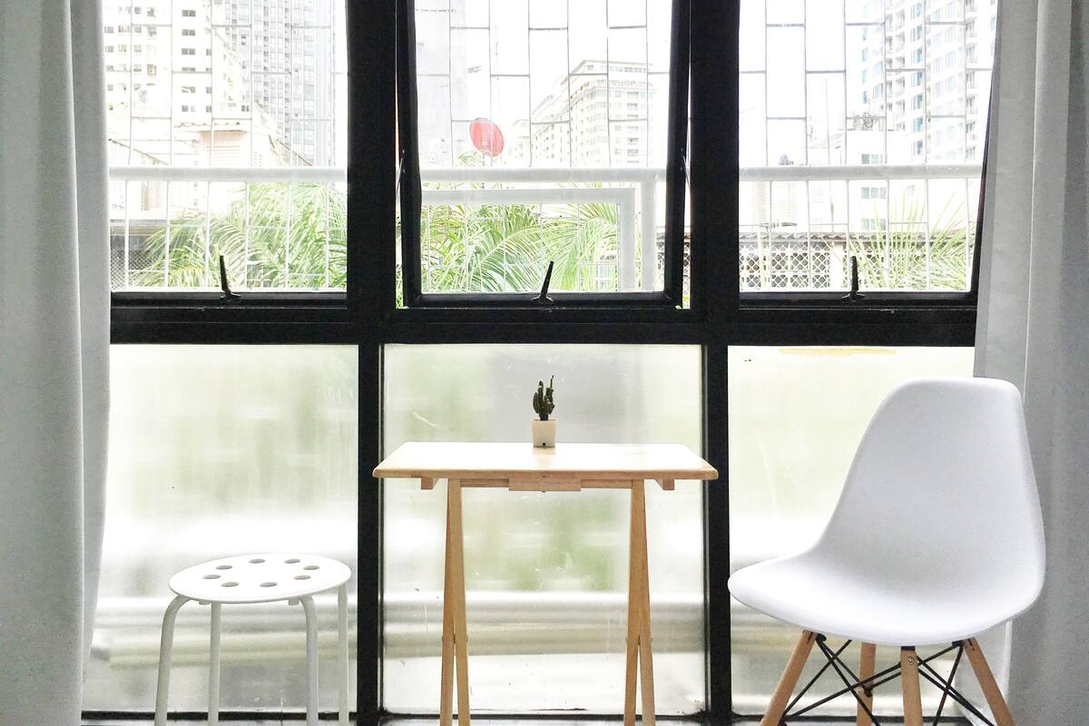 Une pièce avec une grande fenêtre, une petite table en bois, une chaise blanche et une plante en pot.