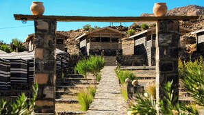 A stone pathway leading to a traditional building with a wooden porch and a pot on top of a stone pillar. - Sama Jabal Shams Resort (Al Hamra)
