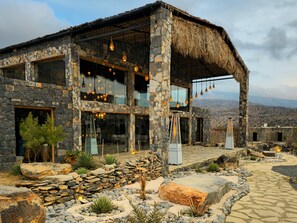 A stone building with large windows, a thatched roof, and hanging light fixtures. - Sama Jabal Shams Resort (Al Hamra)