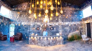 A stone-walled interior with a hanging light fixture, a clock, and a wooden counter with chairs around it. - Sama Jabal Shams Resort (Al Hamra)