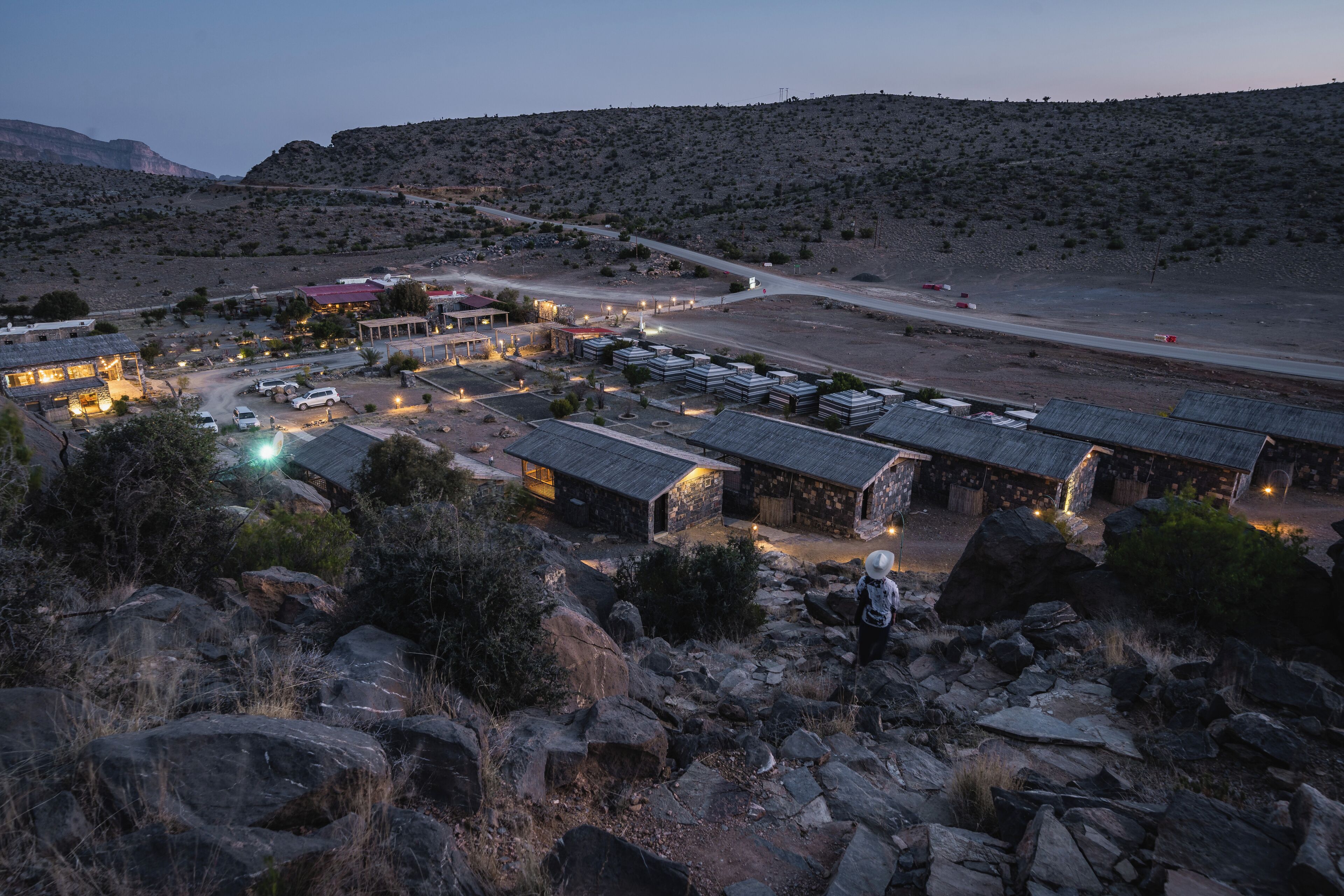 A remote, rustic lodging area with stone buildings, a paved road, and sparse vegetation.