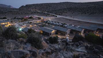A remote, rustic lodging area with stone buildings, a paved road, and sparse vegetation.