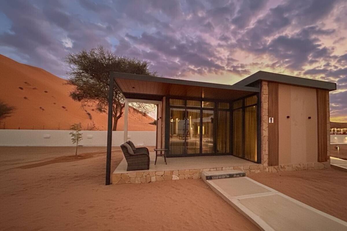 A modern building with a covered patio area, a glass entrance, and a desert landscape in the background.
