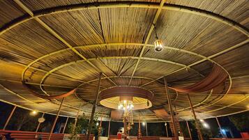 An open-air pavilion with a curved roof structure, seating areas, and hanging light fixtures.