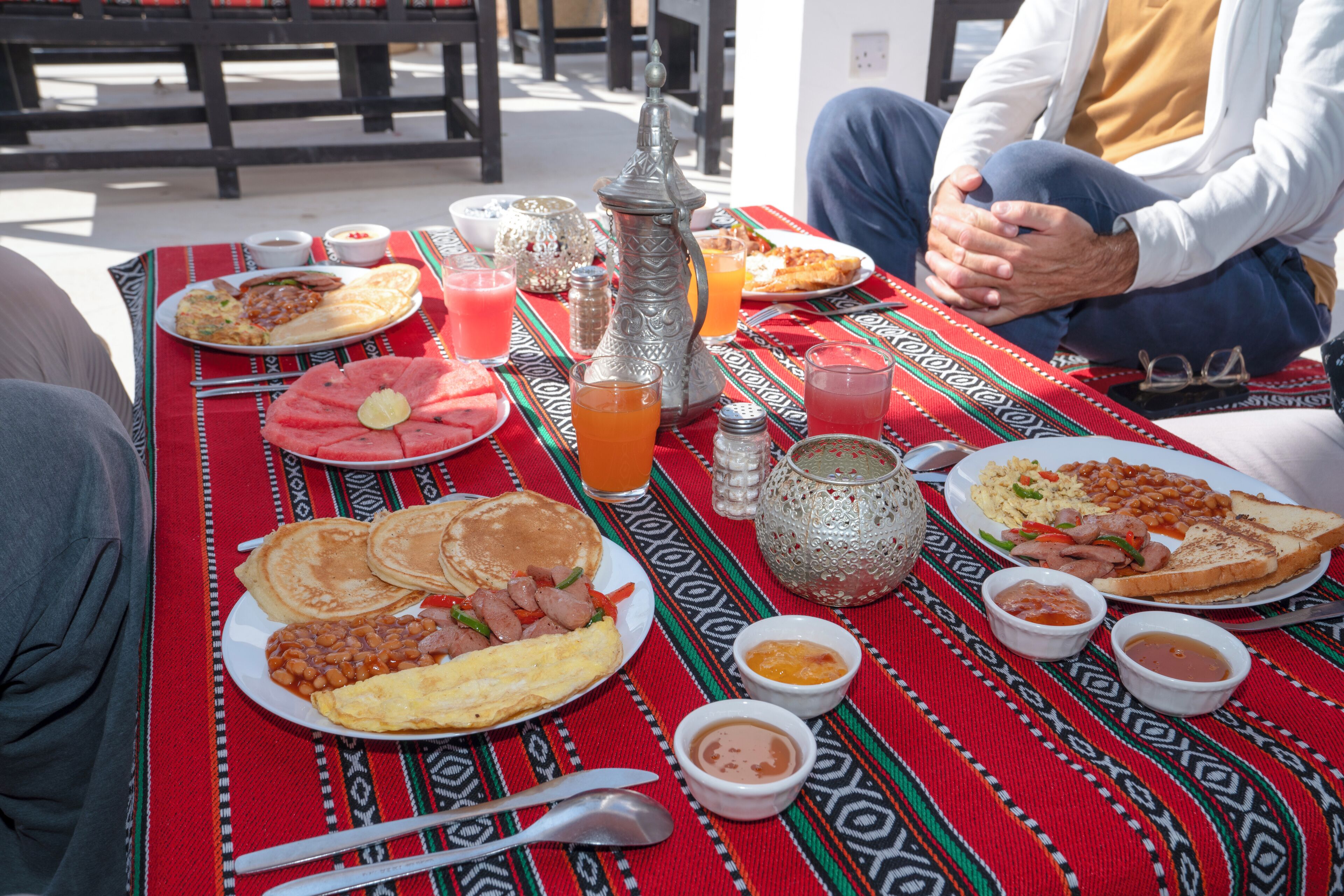 A table set with various breakfast items including pancakes, eggs, beans, and toast, with a patterned tablecloth.