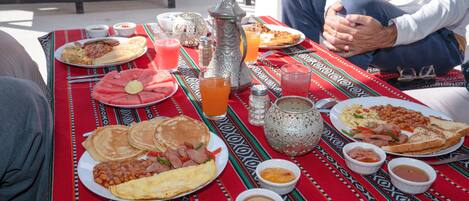 A table set with various breakfast items including pancakes, eggs, beans, and toast, with a patterned tablecloth.