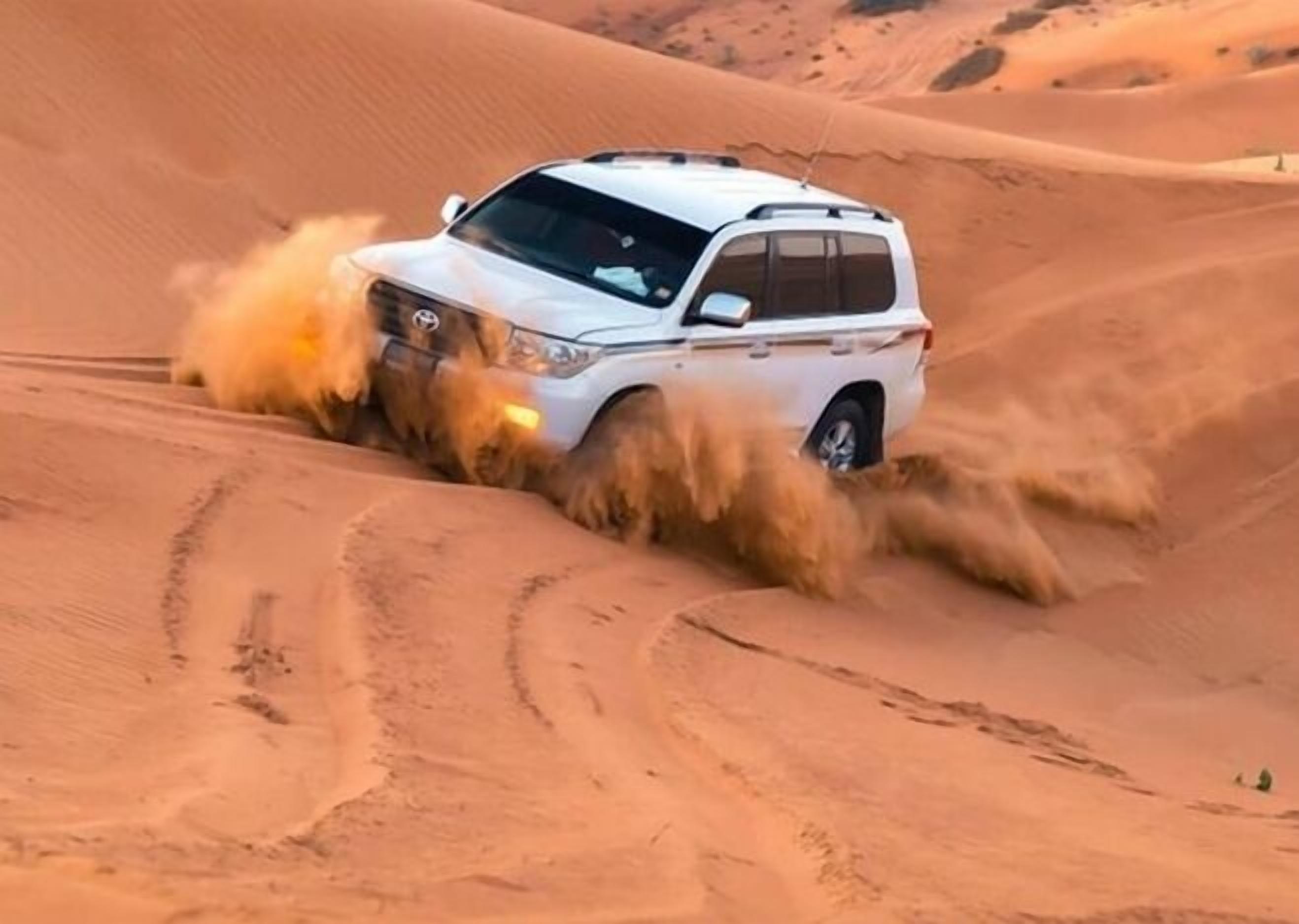 A white SUV navigating through a desert landscape with sand dunes.