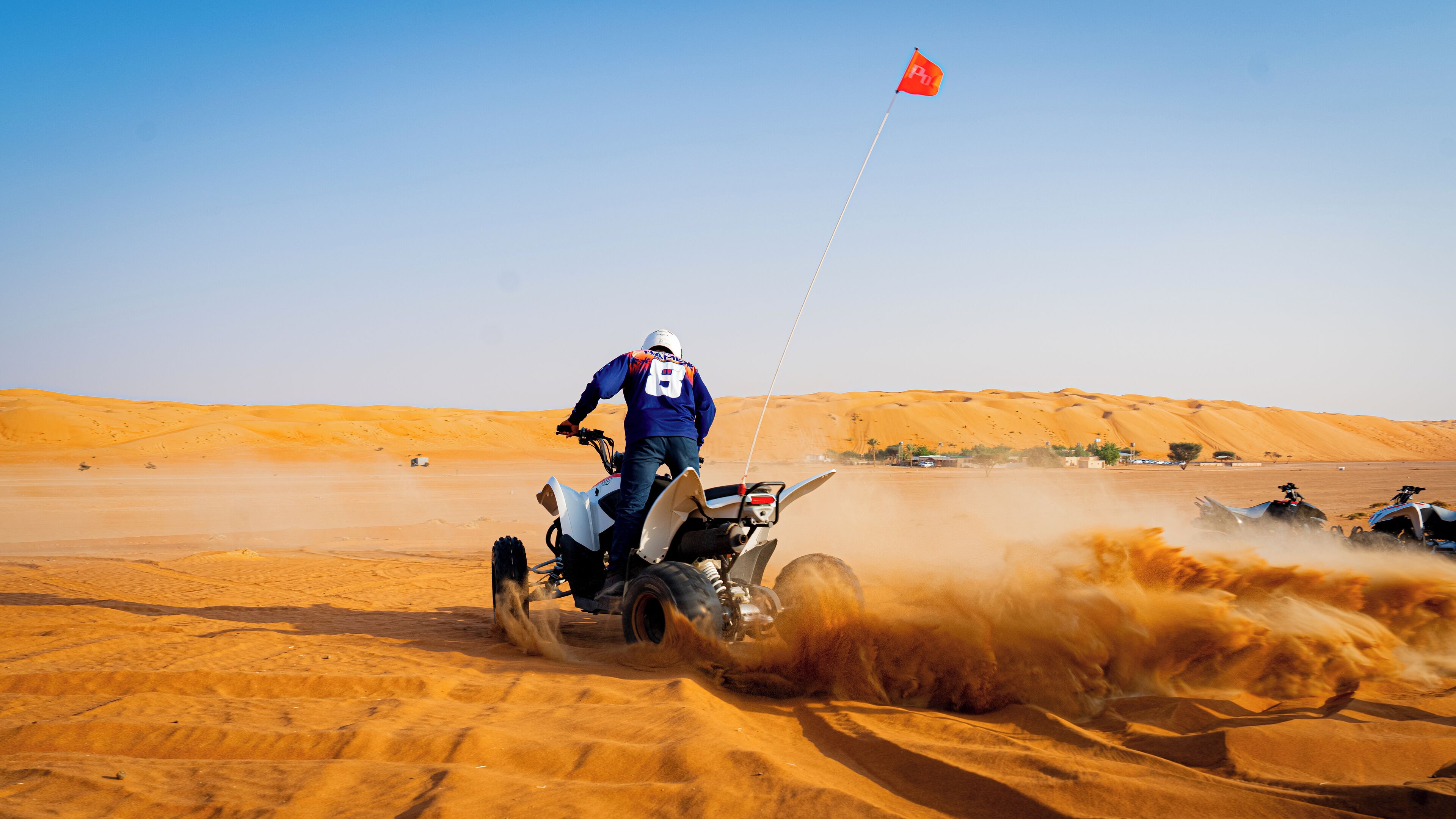 A desert landscape with sand dunes and a person riding an ATV.