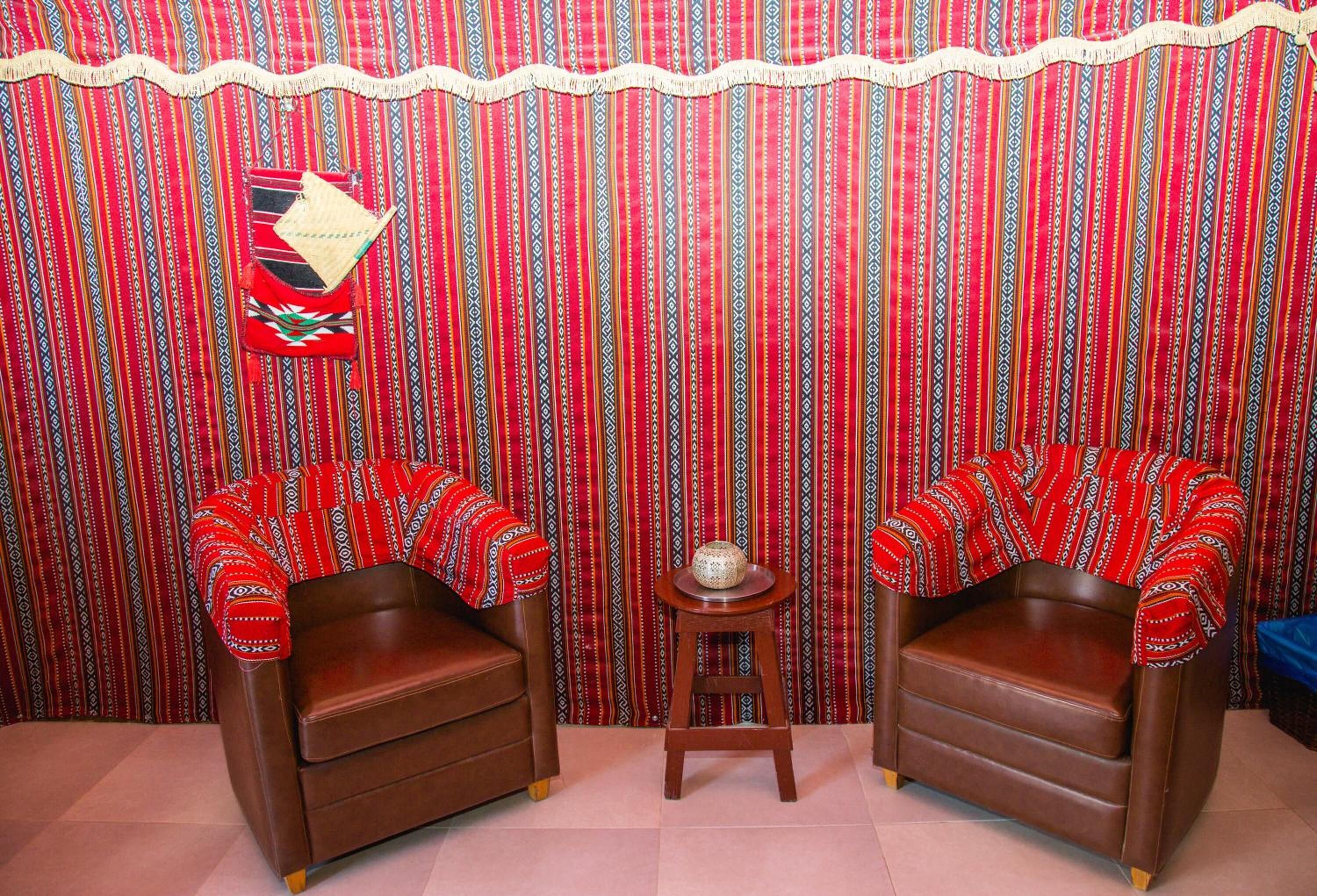 A room with two brown leather armchairs, a small wooden stool, and a patterned curtain backdrop.