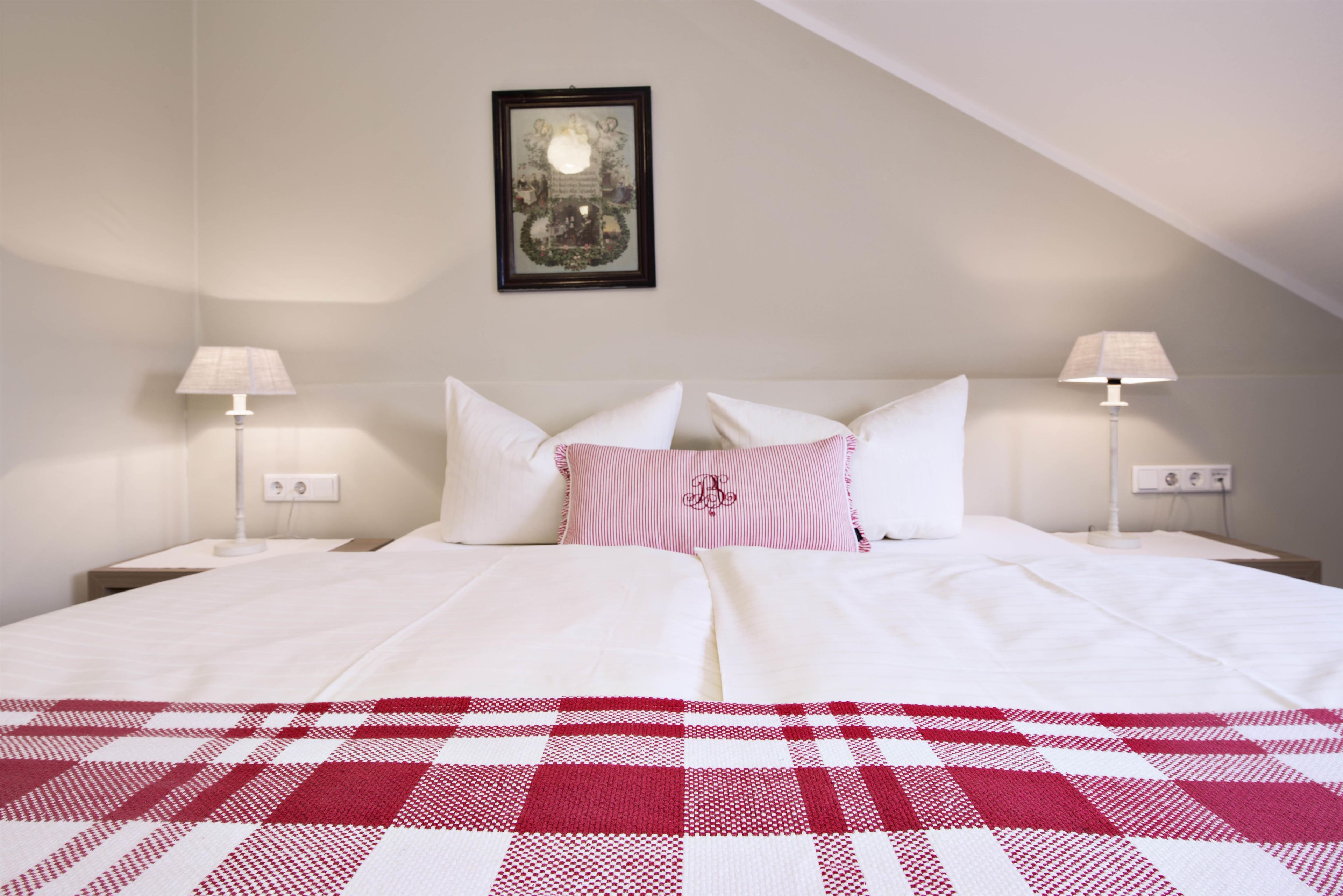 A hotel room with a bed, two bedside lamps, a framed picture on the wall, and a checkered blanket.
