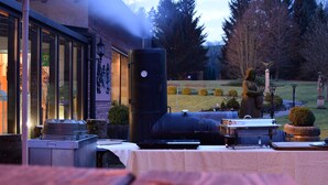 Un área de comedor exterior con una parrilla, mesas y una estatua.