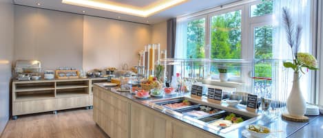 A modern breakfast bar with a variety of food options, a wooden cabinet, and a window with a view of greenery.