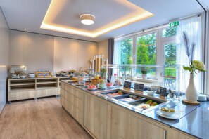 Una barra de desayuno moderna con diversas opciones de comida, un mueble de madera y una ventana con vista a la vegetación.