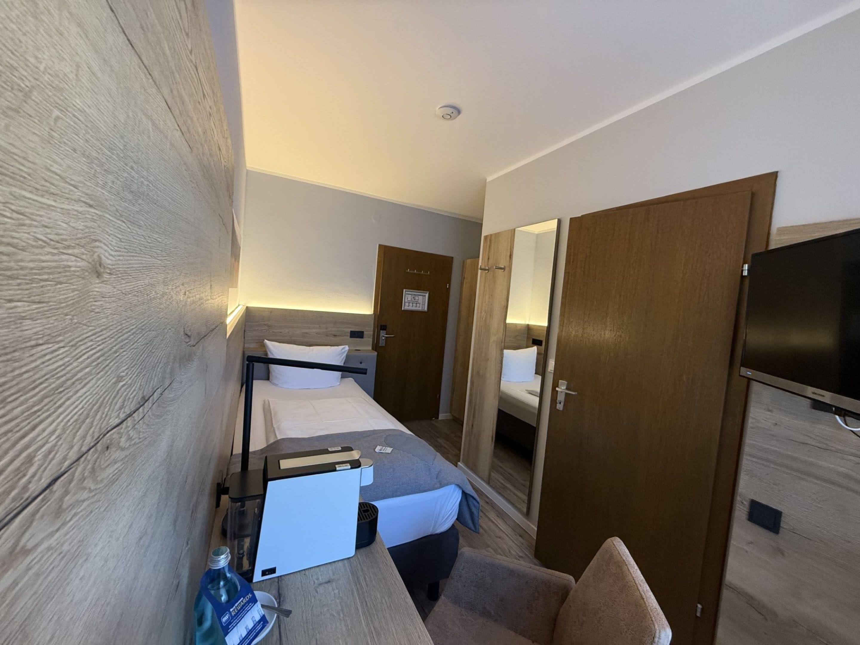 A hotel room with a bed, a desk, a chair, a television, and a wardrobe.