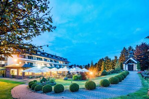 Un patio de hotel con setos bien cuidados, asientos exteriores y un edificio con varios balcones.