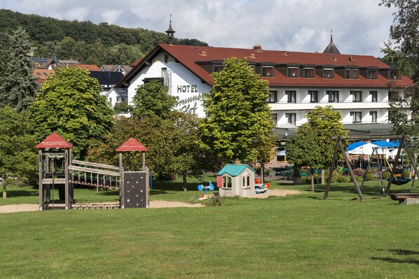 Un hotel con techo rojo, un parque infantil con un tobogán y una casita de juegos.
