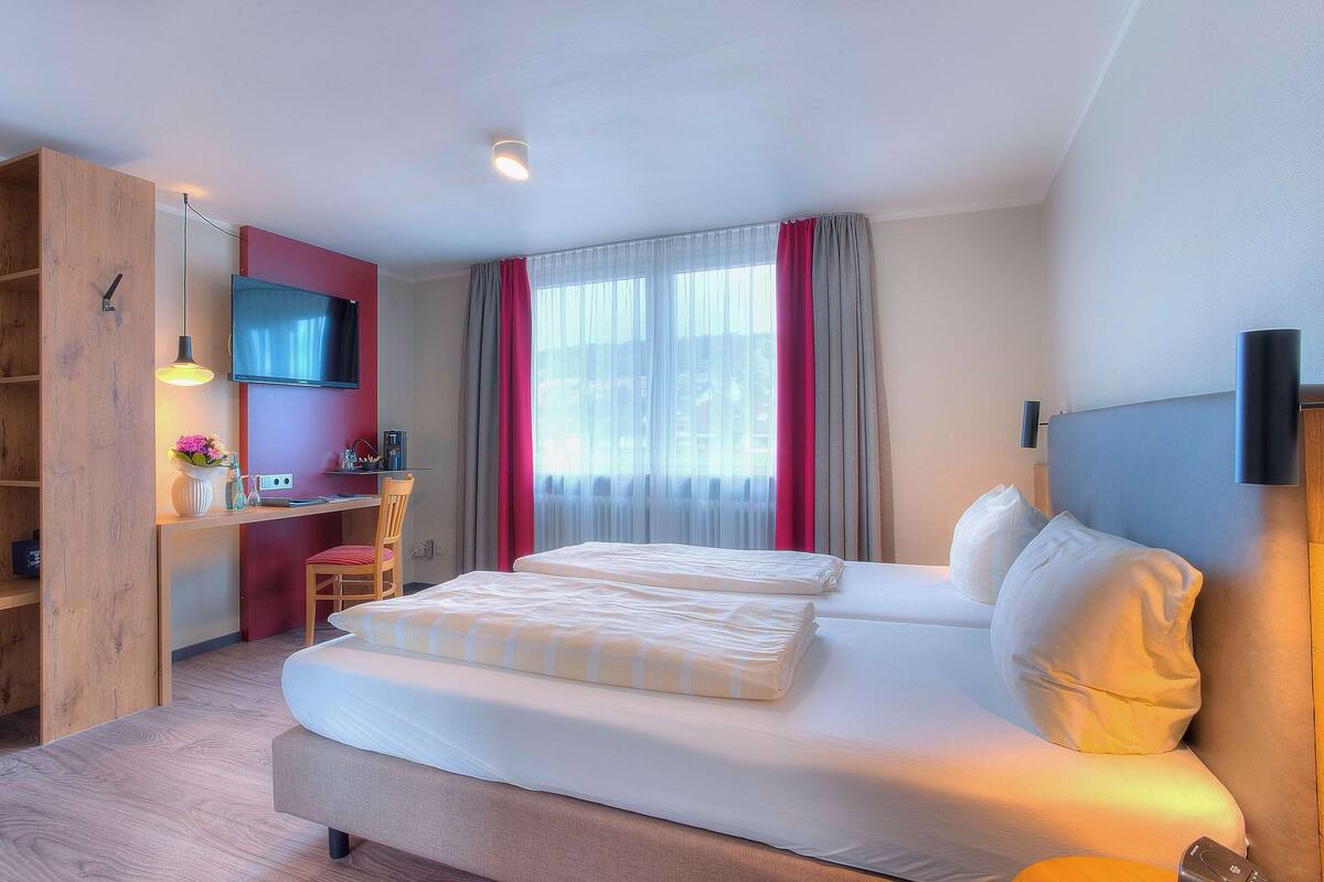 A hotel room with a bed, a desk with a computer, a TV, and a wardrobe.