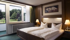 Una cama doble con dos mesitas de noche, una ventana con cortinas, un radiador y un cuadro en la pared.
