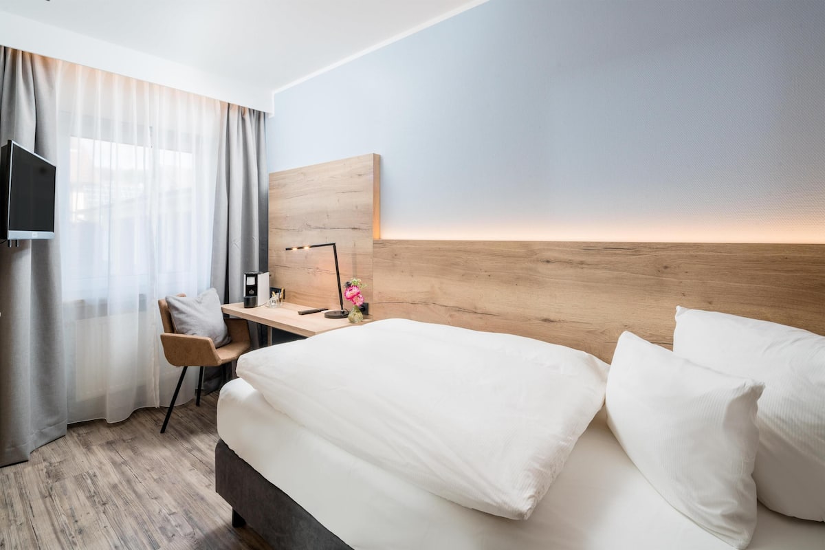 A hotel room with a bed, a desk with a chair, a TV, and a wooden headboard.
