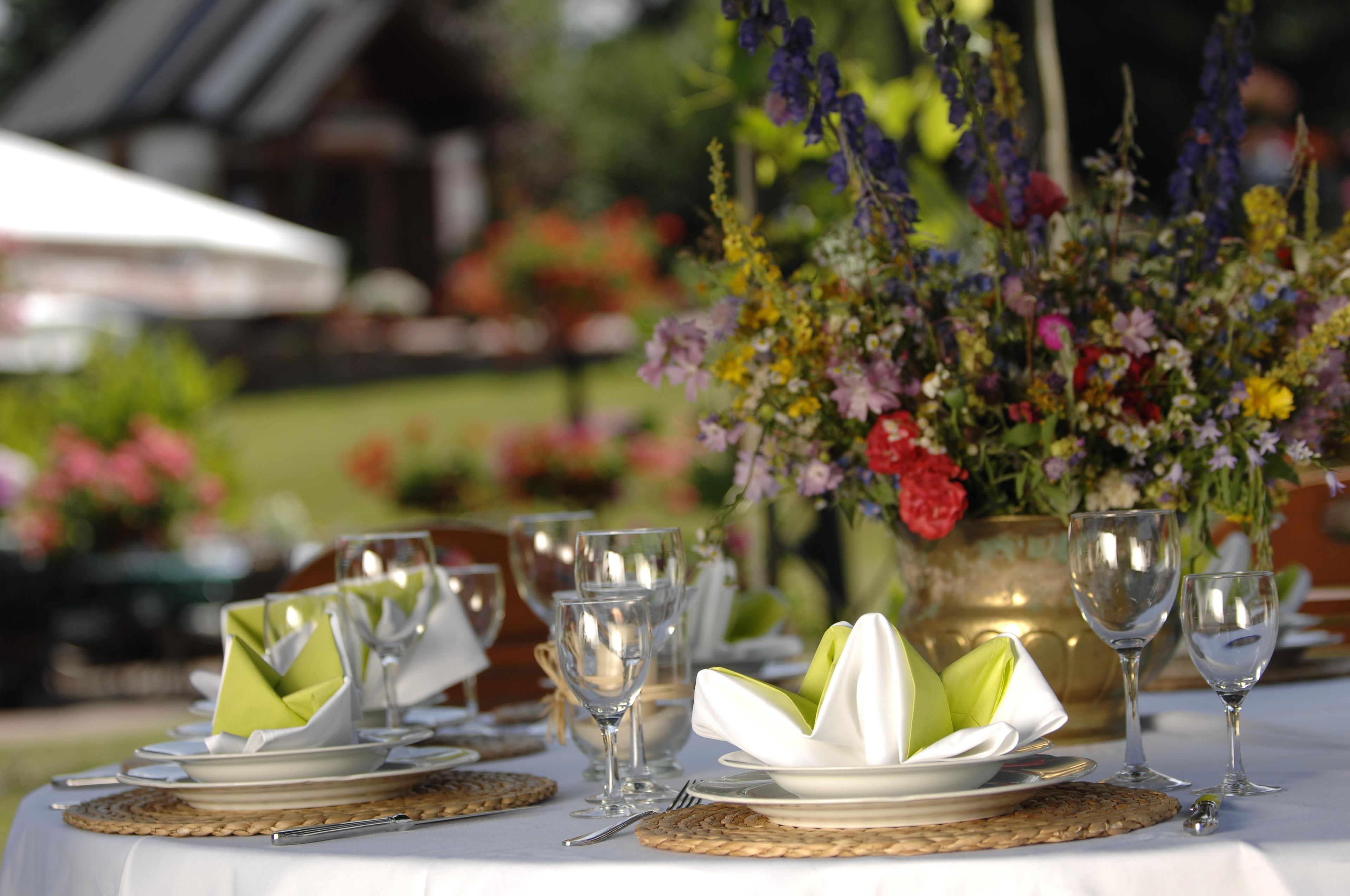 Ein gedeckter Tisch mit Tellern, Besteck und Gläsern, umgeben von einer Blumenkomposition.