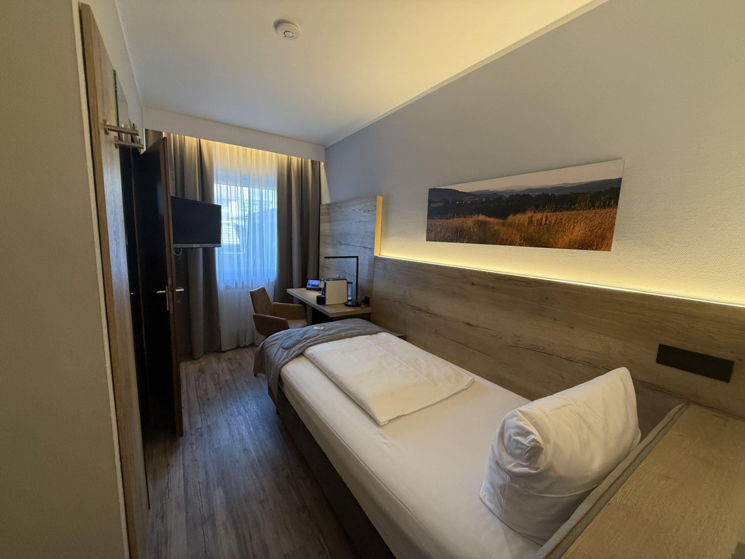A hotel room with a bed, a desk with a computer, a chair, and a television.