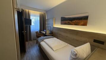 A hotel room with a bed, a desk with a computer, a chair, and a television.