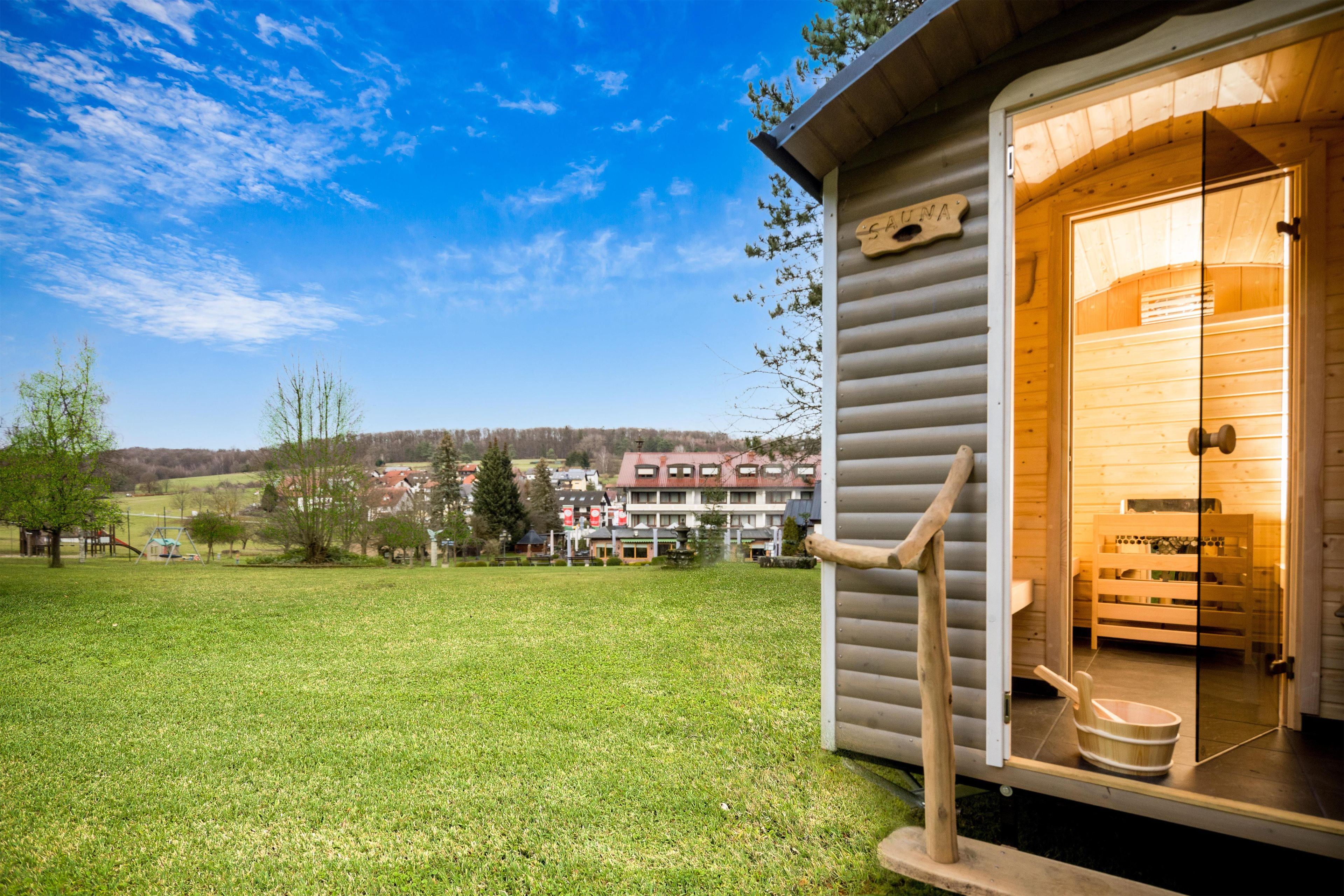 A wooden cabin with a door open, revealing a sauna room with wooden benches and a bucket.