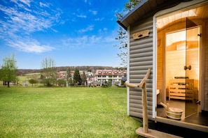 Una cabaña de madera con la puerta abierta, mostrando un espacio de sauna con bancos de madera y un balde.